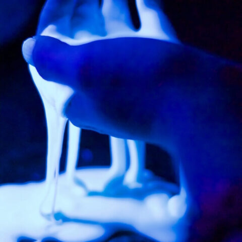 Glowing slime dripping from a hand in black light.