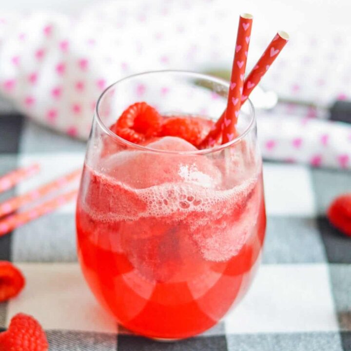 Pink champagne float with raspberries and sorbet on a checkered surface.
