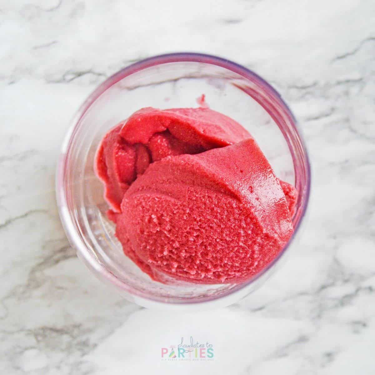 Two scoops of raspberry sorbet in a glass.