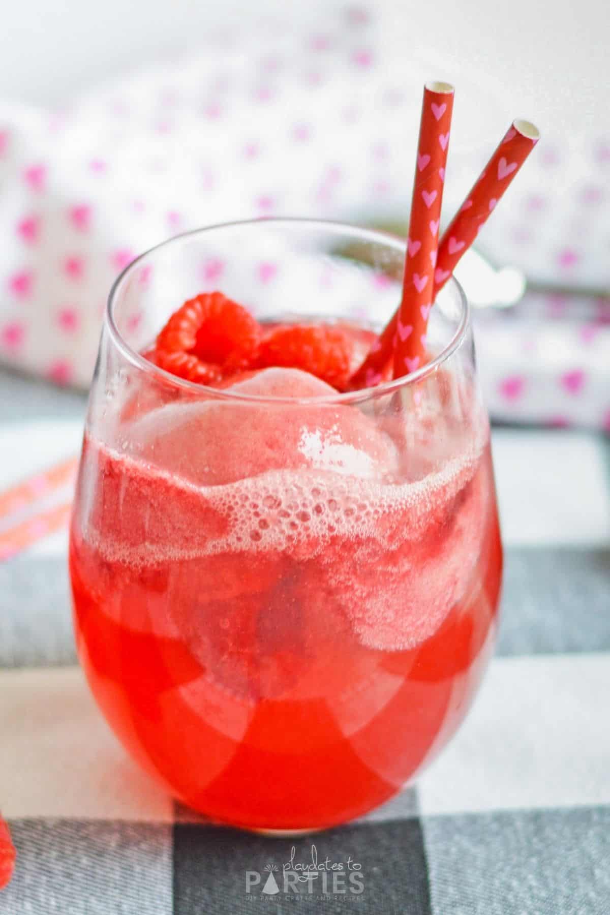 A finished raspberry sorbet champagne float cocktail with red straws and fresh fruit.