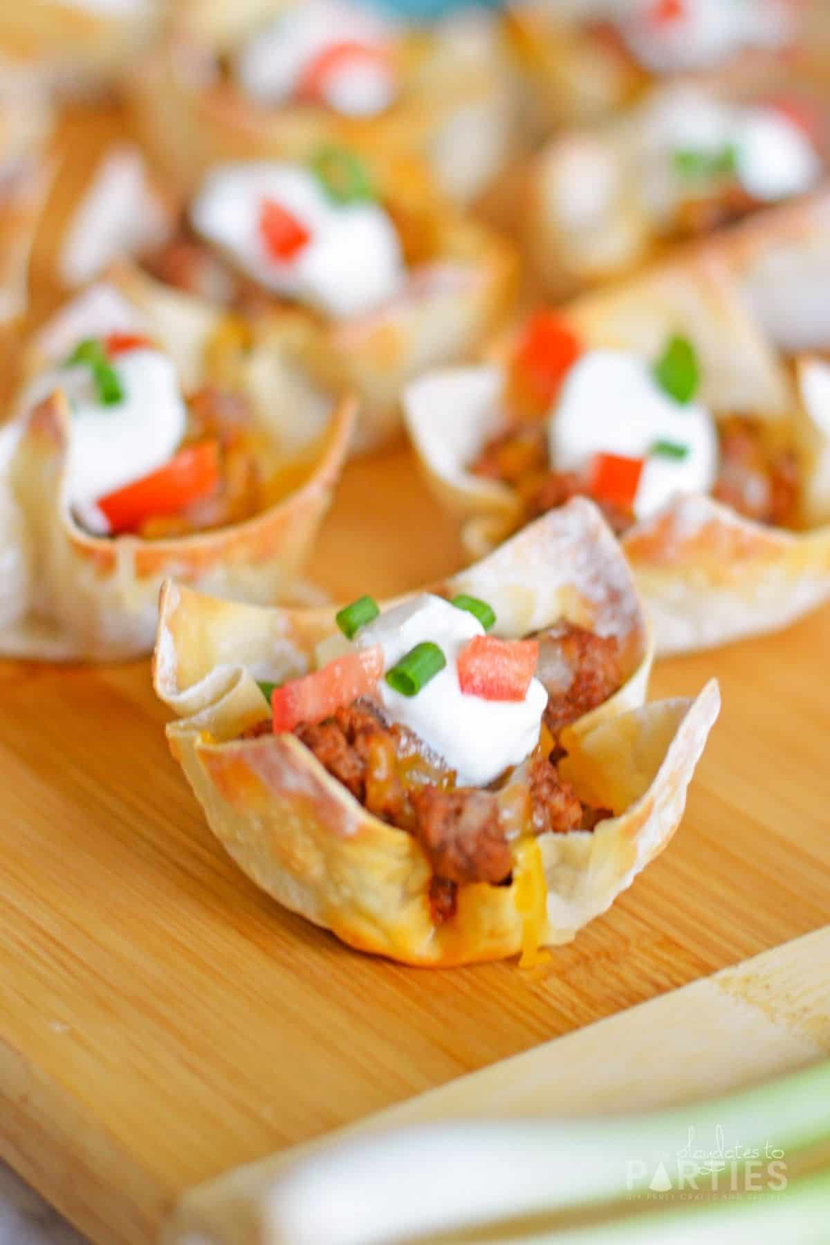 Close up of the side of a mini taco cupcake with sour cream, tomato, and green onion.
