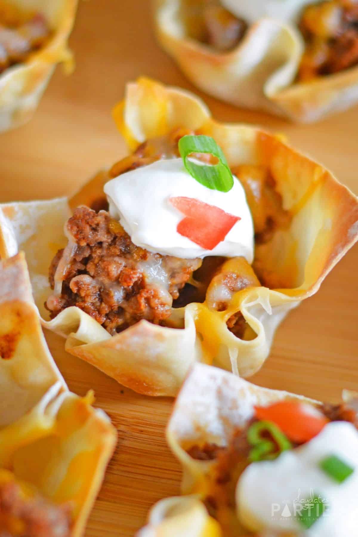 Close up view of a wonton taco cup filled with seasoned beef, cheese, and taco toppings.