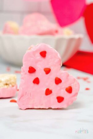 Heart shaped rice krispie treat dipped with pink candy melts and heart shaped sprinkles.