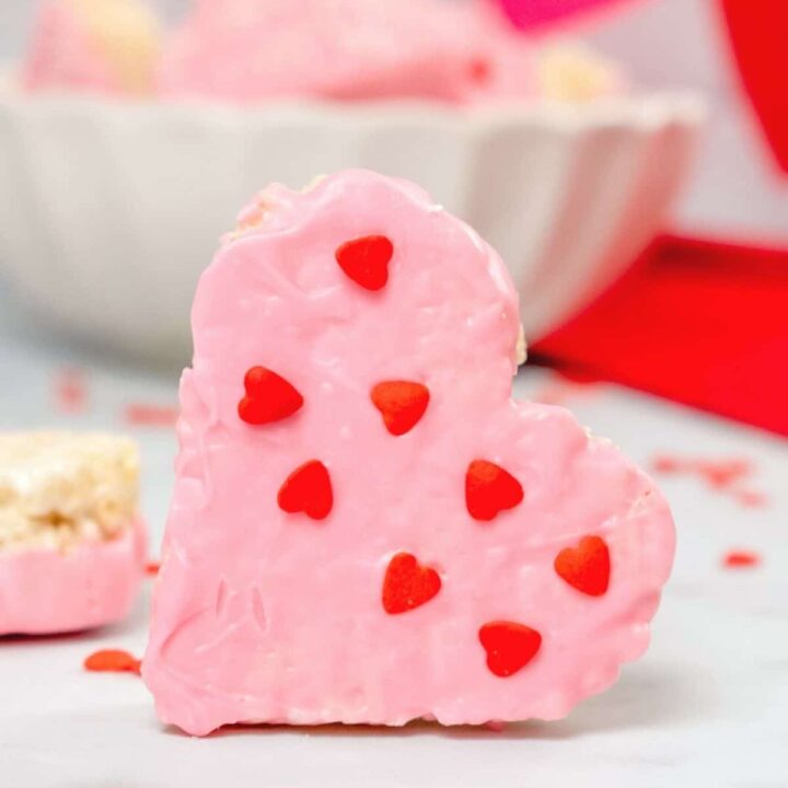 Heart shaped rice krispie treat dipped with pink candy melts and heart shaped sprinkles.