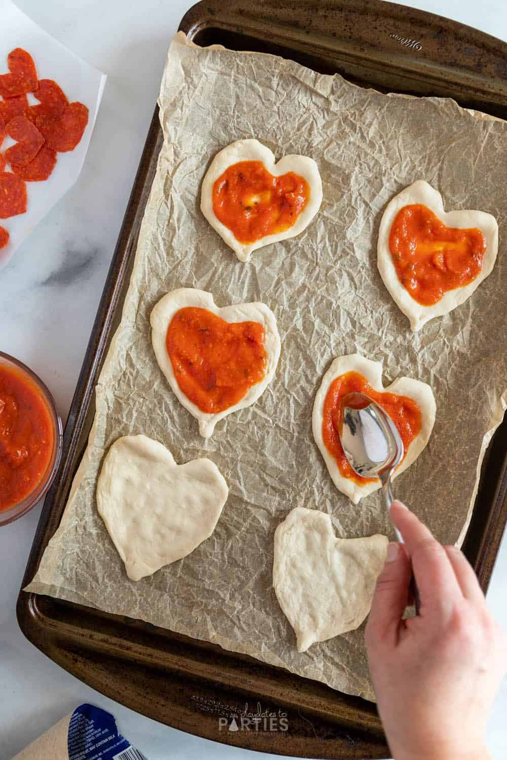 Adding sauce to mini heart shaped pizzas for Valentine's Day.