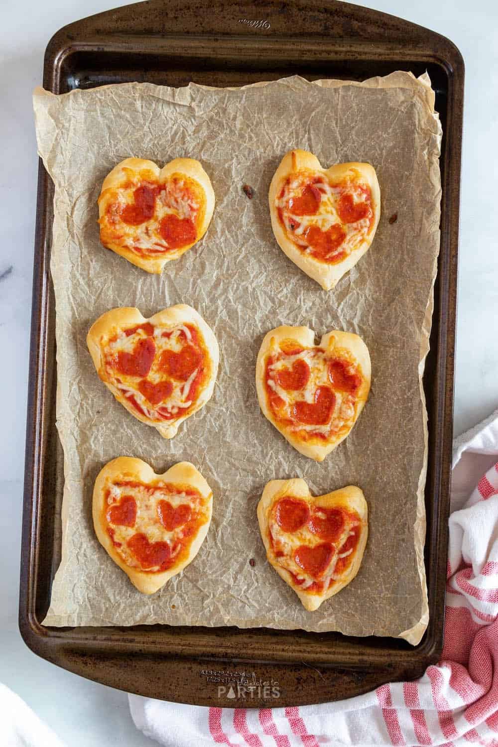 Mini heart shaped pizzas on a pan that are ready to eat.