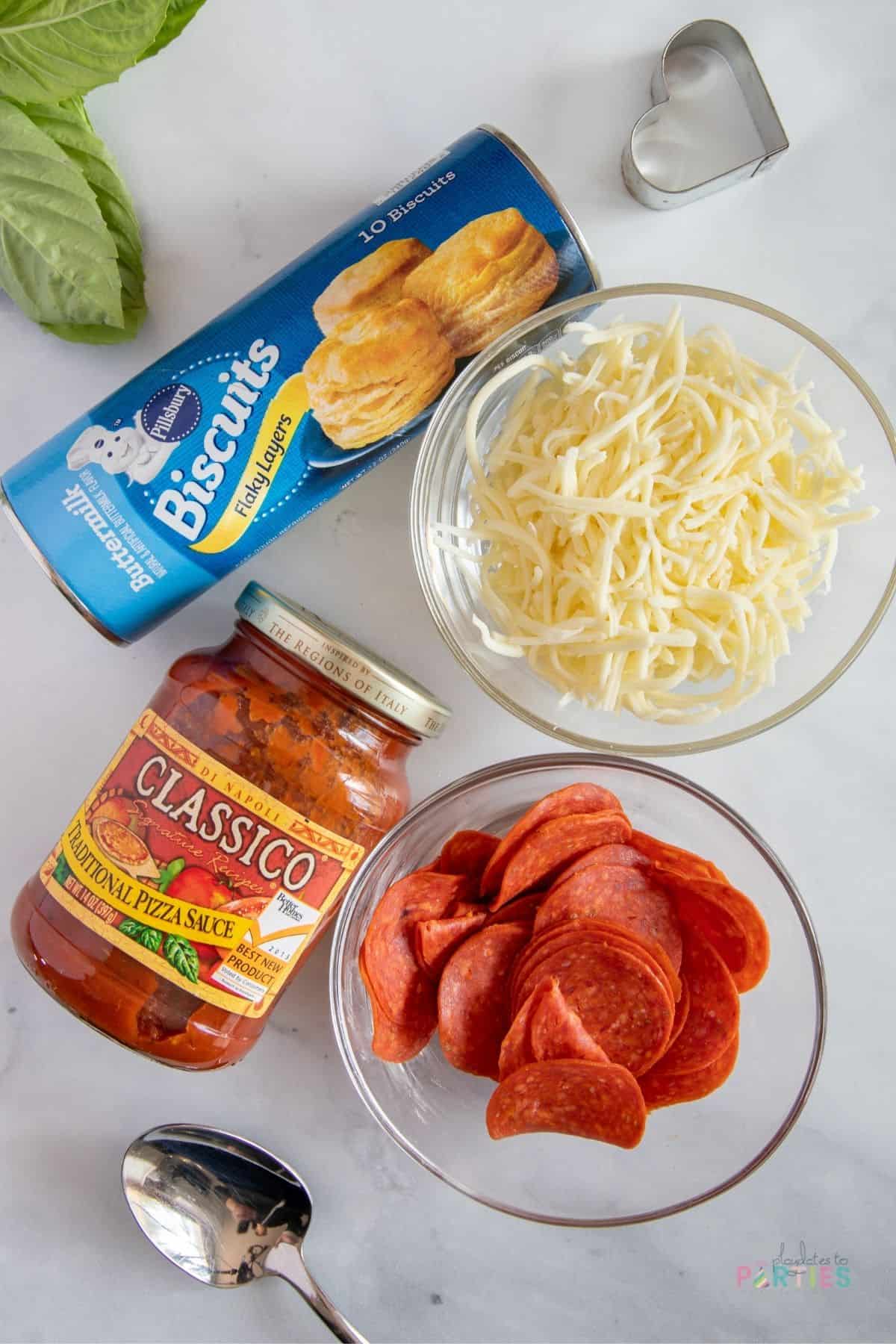 Ingredients for mini heart shaped pizza: biscuit dough, pizza sauce, mozzarella cheese, and pepperoni slices.