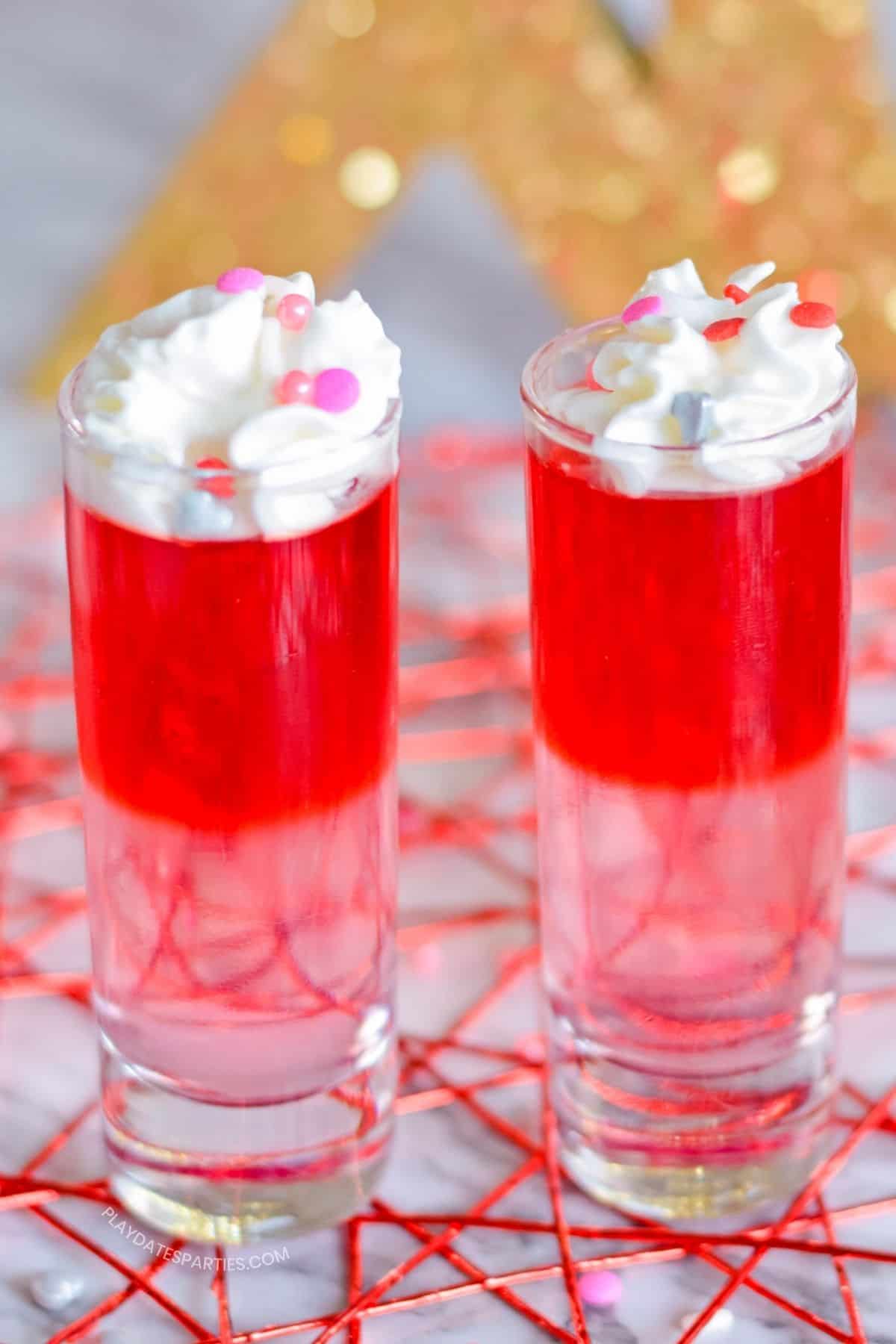 Pink and red layered Valentine's Day jello shots with whipped cream.