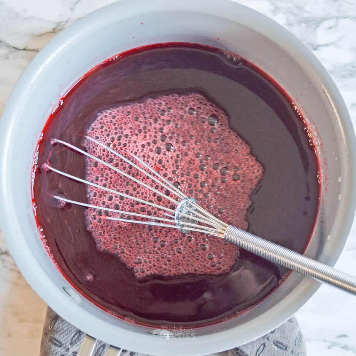 Cherry gelatin mixture in a bowl with a whisk.