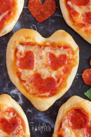Overhead view of mini heart shaped pizza on a dark surface.