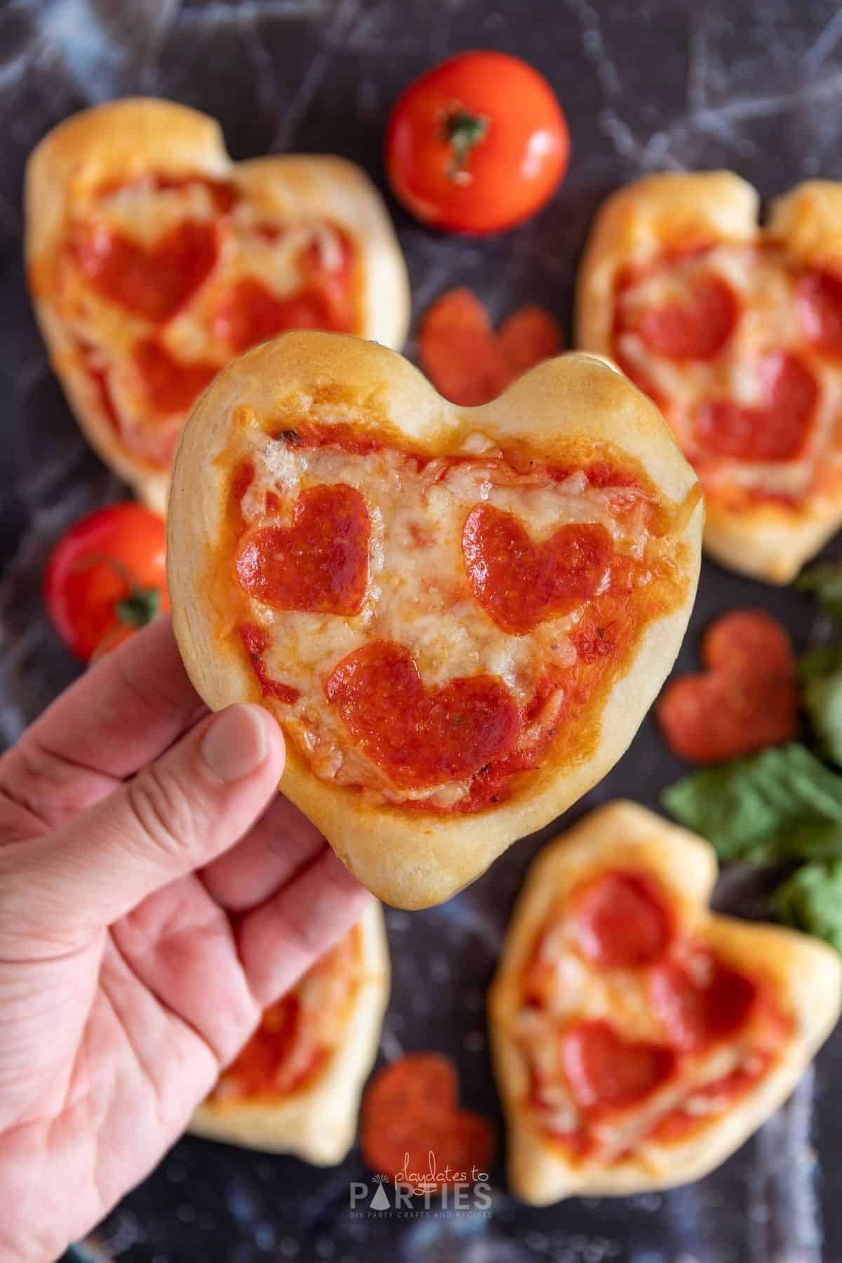 A woman's hand holding a Valentine heart shaped pizza.