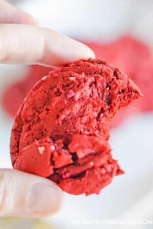 A woman's hand holding a red velvet cookie with a bite taken out.