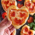 A woman's hand holding a mini heart shaped pizza for Valentine's Day.