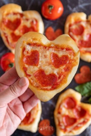 A woman's hand holding a mini heart shaped pizza for Valentine's Day.