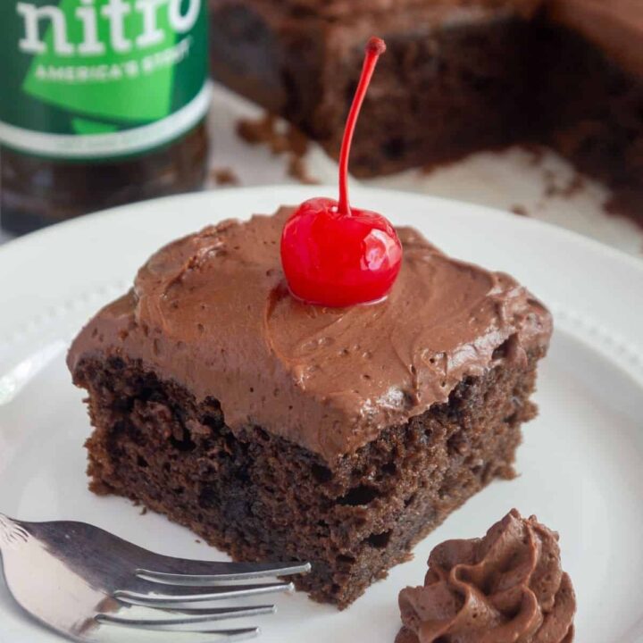 A slice of chocolate sheet cake on a plate in front of a bottle of beer.