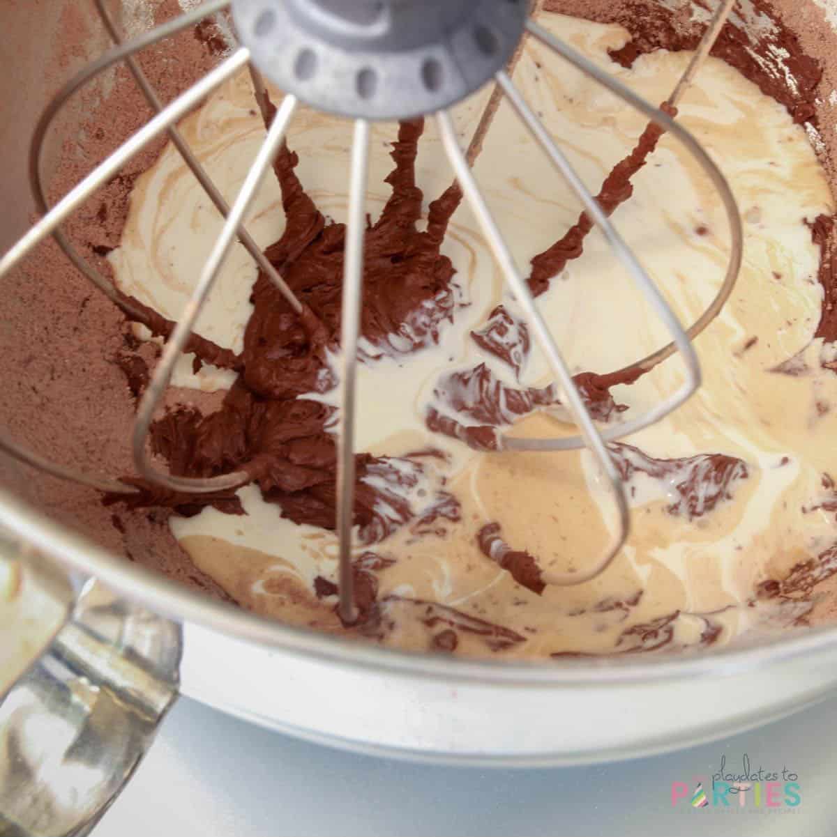 Close up of ingredients for chocolate whipped cream frosting in a stand mixer.