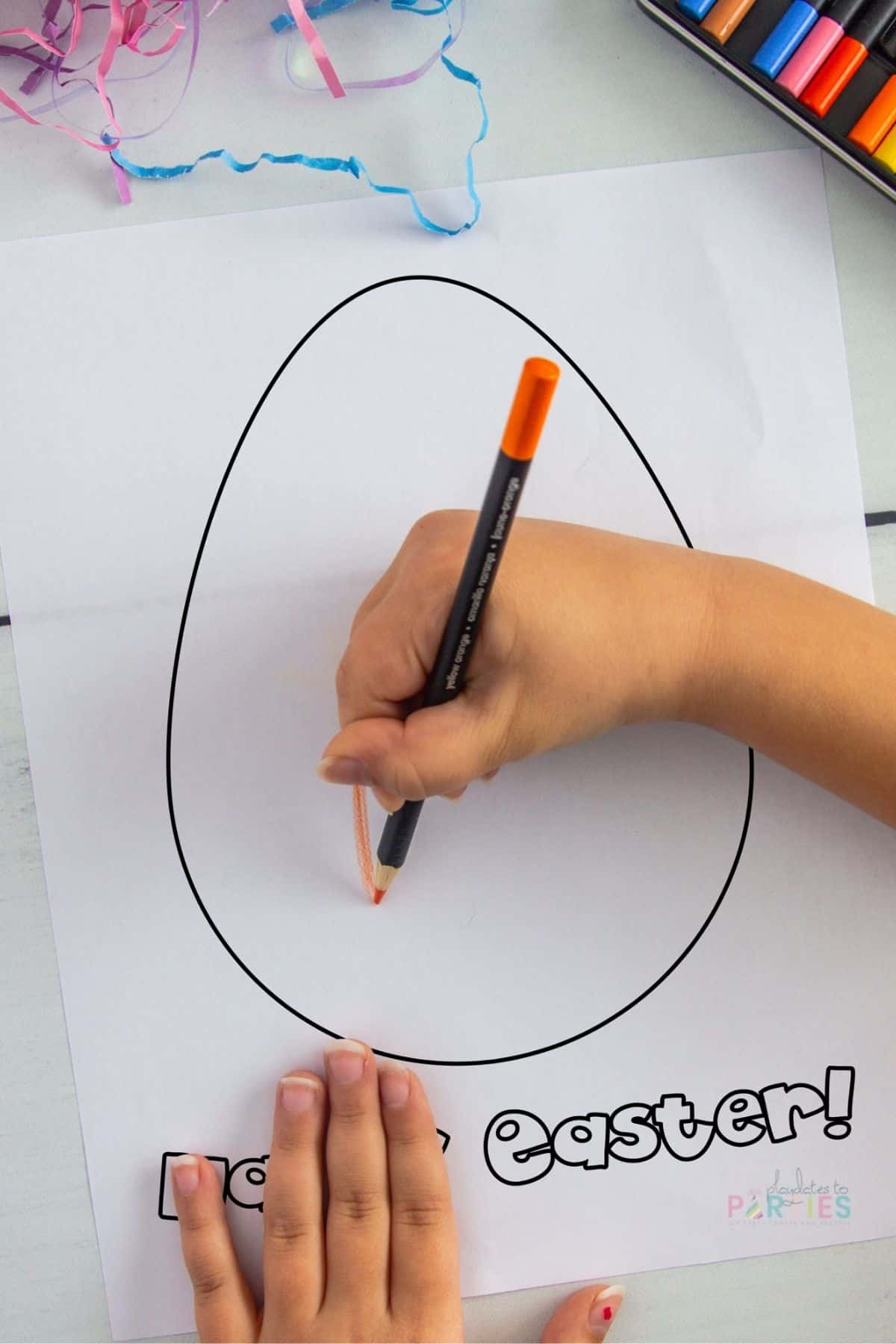 A girl's hand coloring in a page with a blank egg that says Happy Easter underneath.