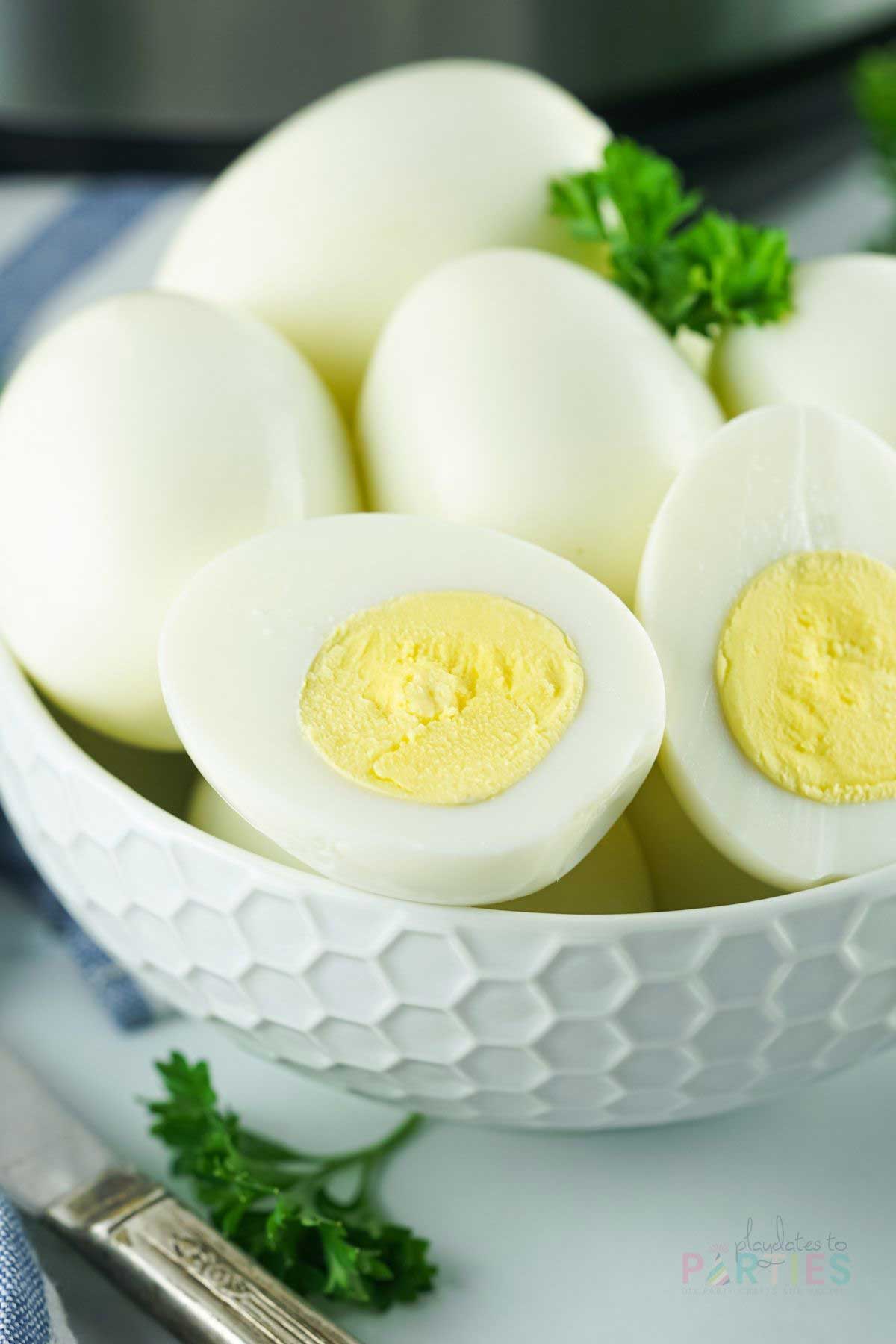Hard boiled eggs in a white bowl, with one egg cut in half to show the yolk.
