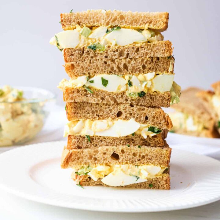 Crustless egg sandwiches stacked high on a plate.