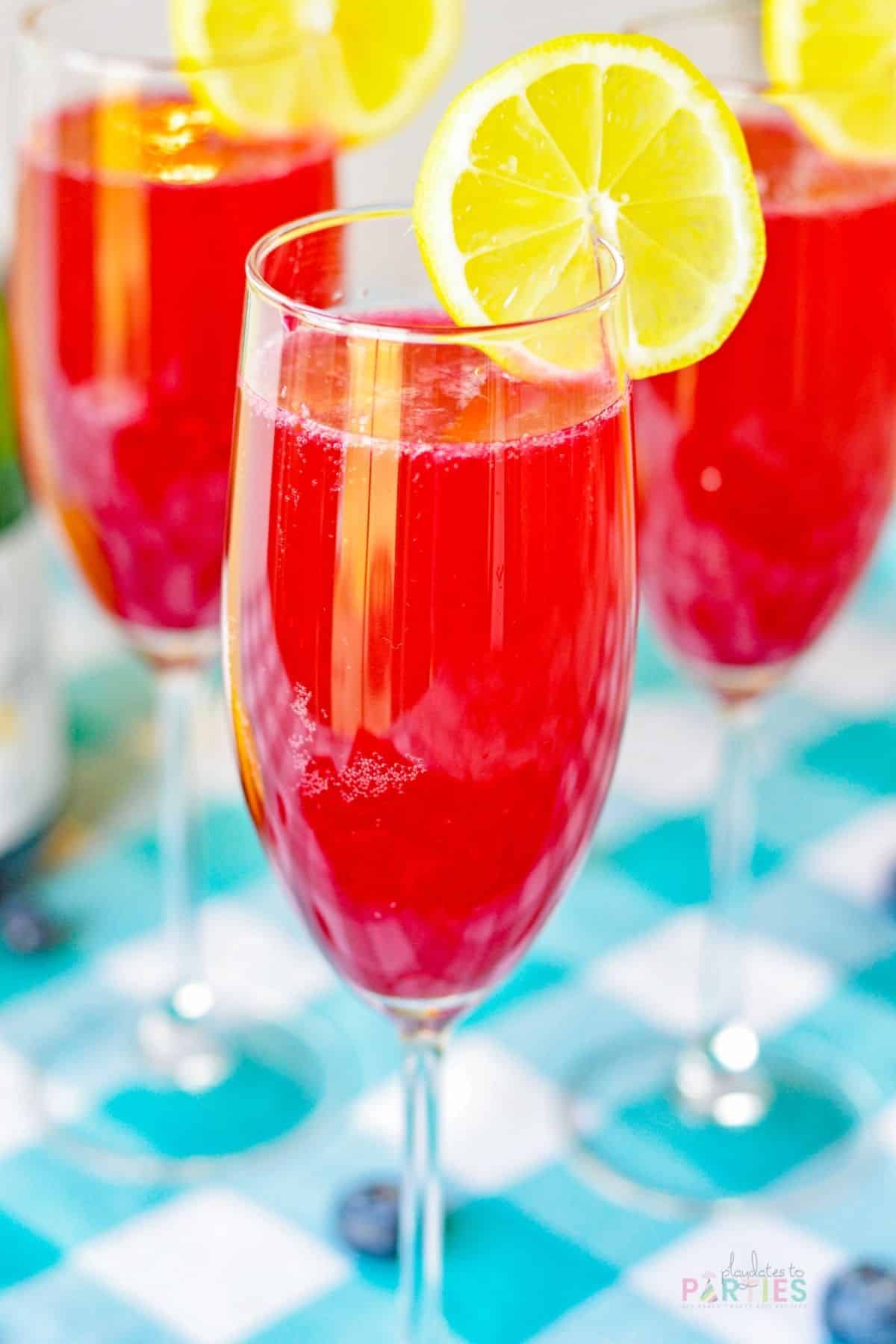 Bright red mimosa in a champagne flute garnished with lemon.