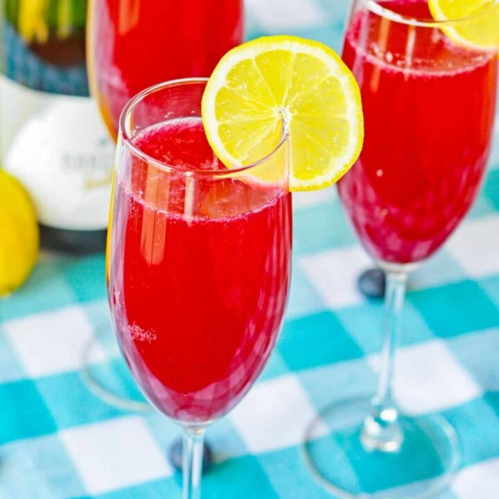 Blueberry lemonade mimosas garnished with lemon slices next to a bottle of champagne.