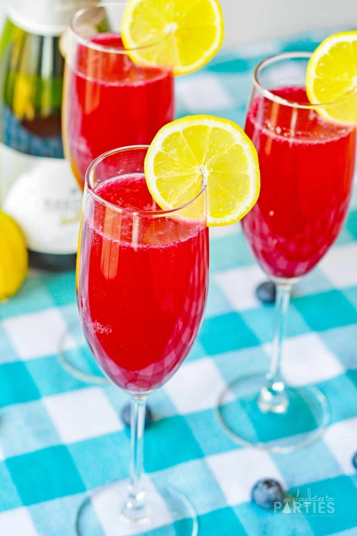 Blueberry lemonade mimosas garnished with lemon slices next to a bottle of champagne.