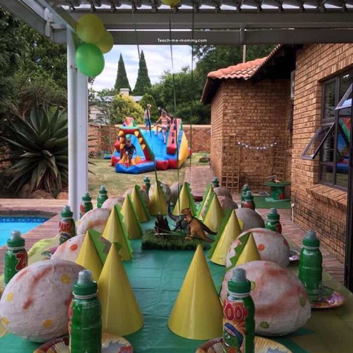 A party table set with giant dinosaur egg pinatas and party hats.
