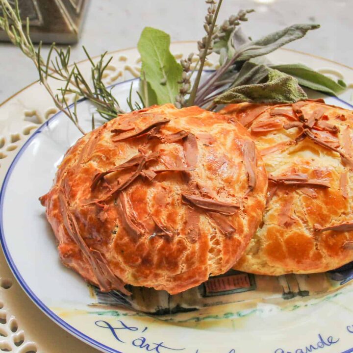 Large gougeres cheese puffs on a decorative plate with fresh herbs as garnish.