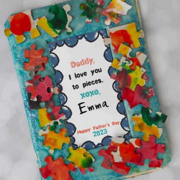 A homemade frame decorated with colored puzzle pieces and a Father's Day gift inside that says I love you to pieces.