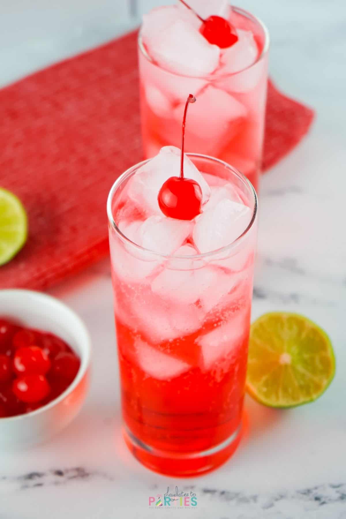 Overhead view of two red drinks surrounded by cherries and limes.