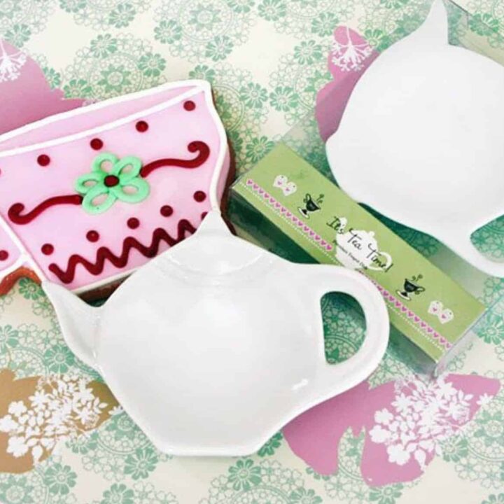 Porcelain teapot shaped tea bag caddy on a floral surface.