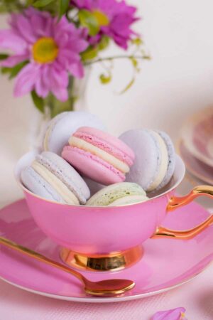 Pink teacup filled with colorful macarons.