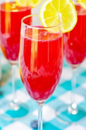 Bright red mimosa in a champagne flute garnished with lemon.