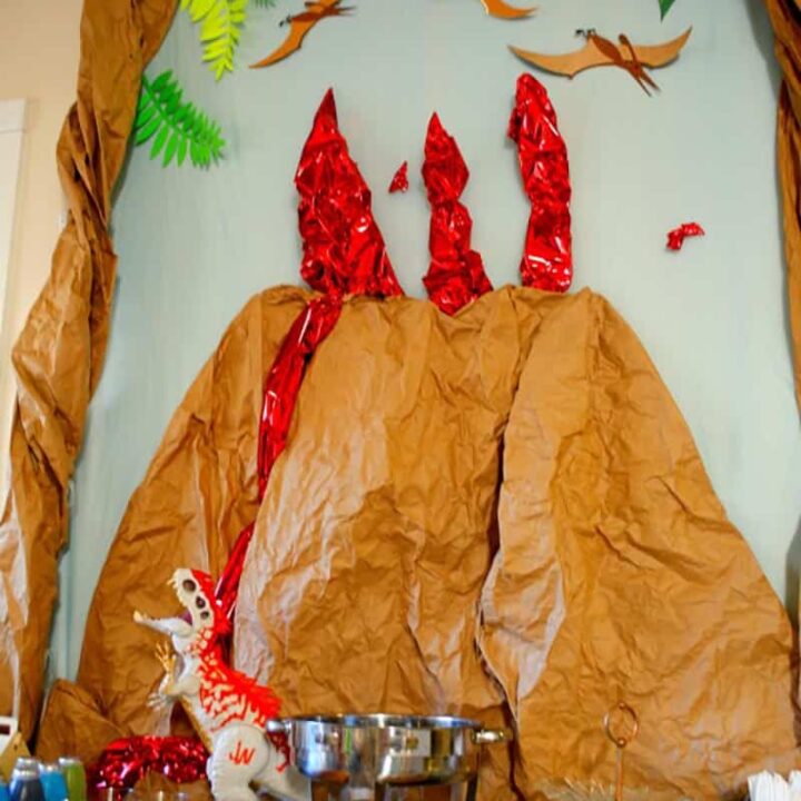 Dinosaur birthday party decorations with a three dimensional volcano backdrop against the wall.