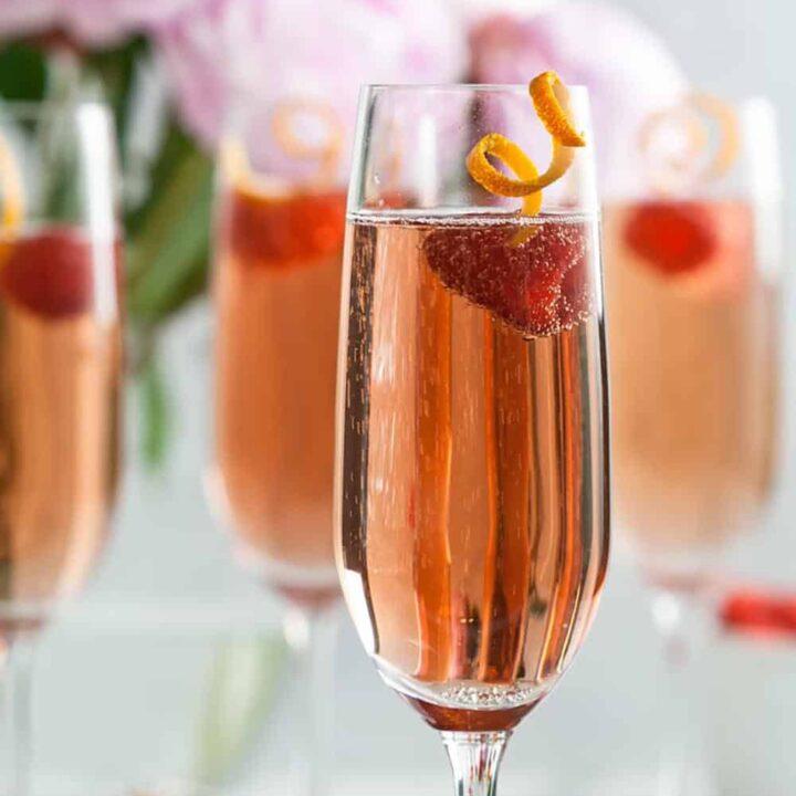 Champagne flutes filled with Kir Royale and garnished with citrus curls and raspberries.