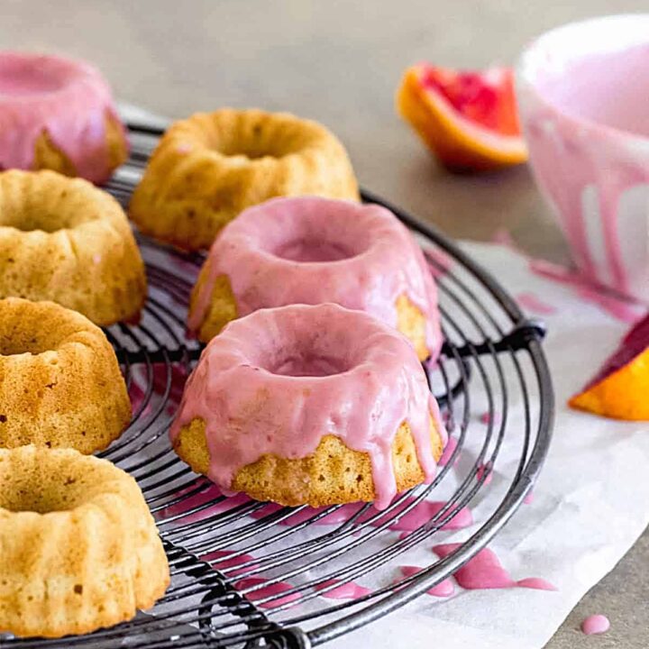 Mini bundt cakes with pink blood orange glaze on a cooling rack.