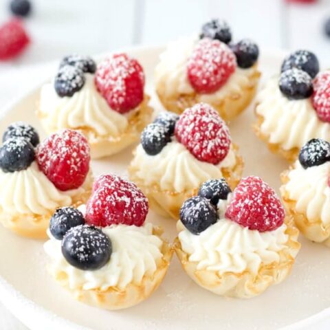 Mini cheesecake bites with blueberries and raspberries on a white plate.