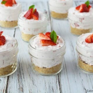 Individual jars filled with strawberry cheesecake and garnished with fresh berries.