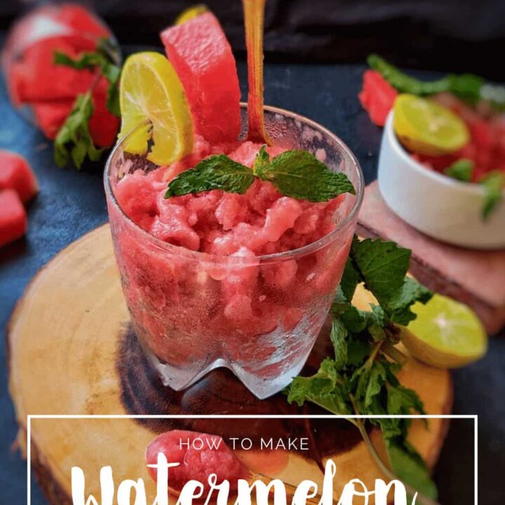 A glass filled with watermelon slushie, garnished with fresh fruit slices and mint.