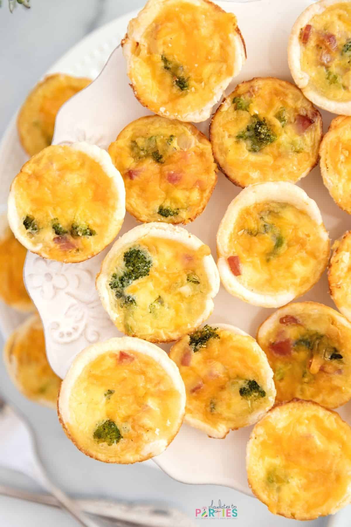 Overhead view of ham and broccoli quiche bites on a tiered white tray.