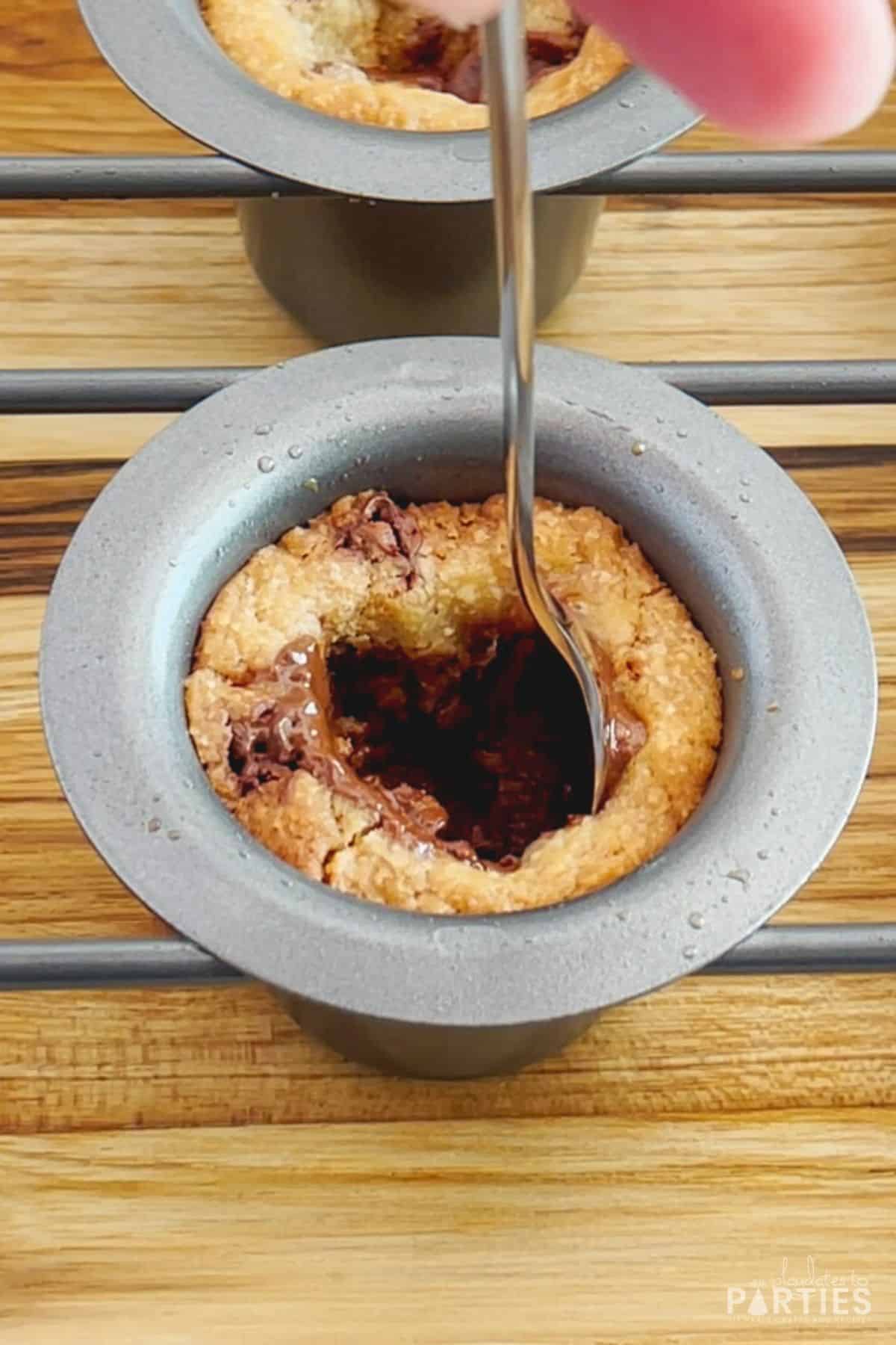 A long handled spoon pressing cookie dough against a popover pan mold.