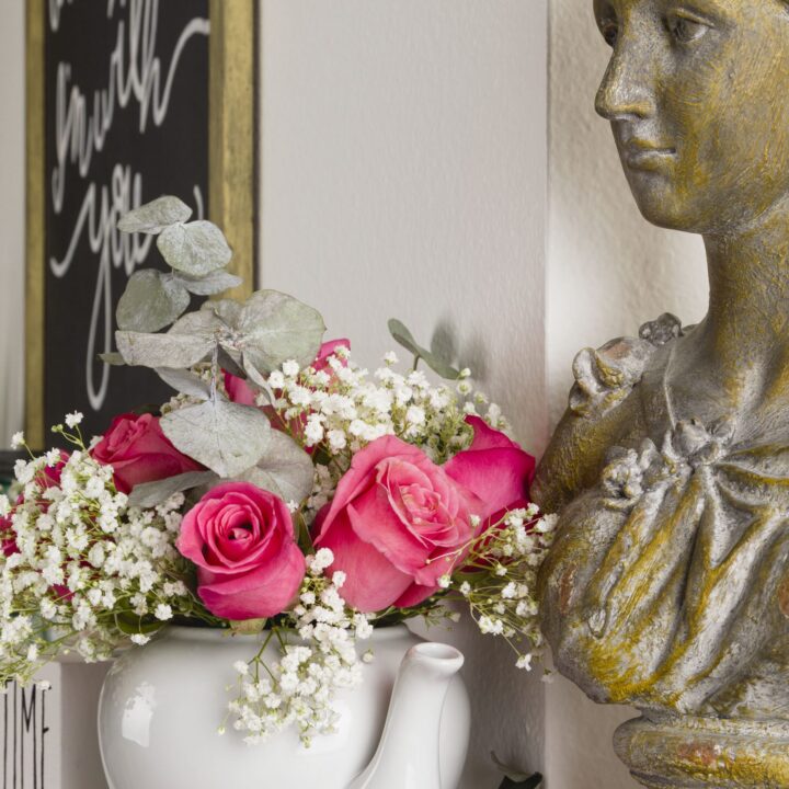A flower arrangement of roses and baby's breath in a white teapot.