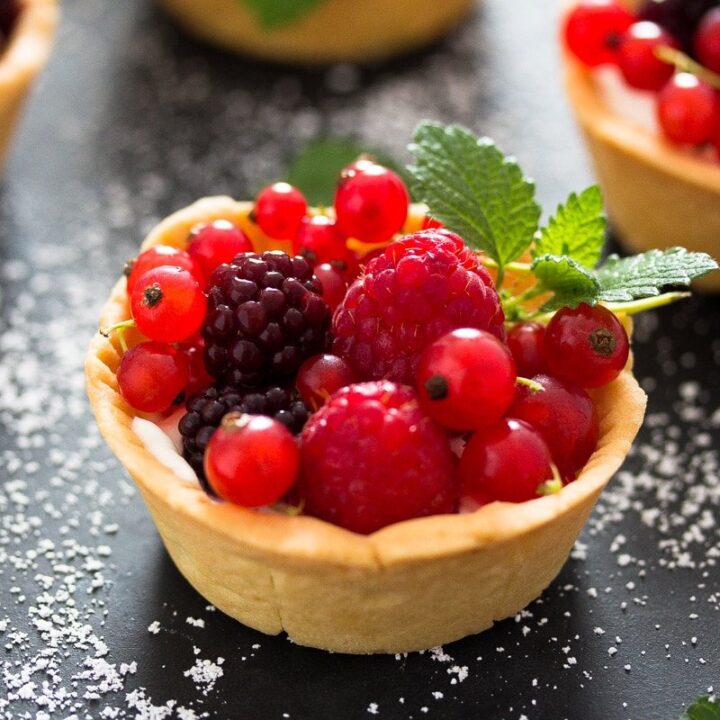 A miniature tart on a dark surface filled with a variety of berries.