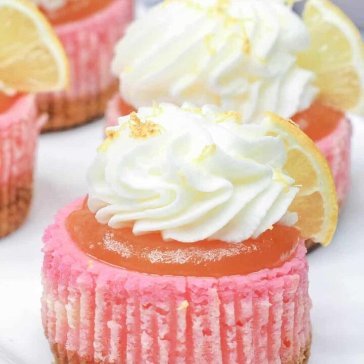 A miniature pink lemonade cheesecake with whipped cream and fresh lemon wedges.