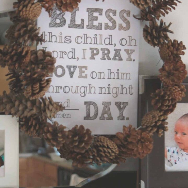 A wreath made out of pine cones with subway art inside for a baby boy baptism reception.
