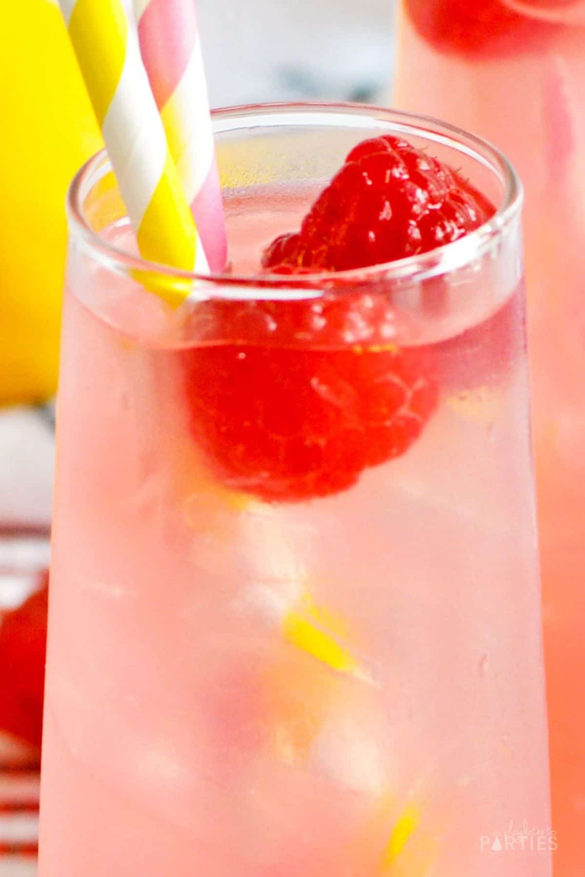 Close up view of a pink lemonade drink garnished with paper straws and fresh raspberries.