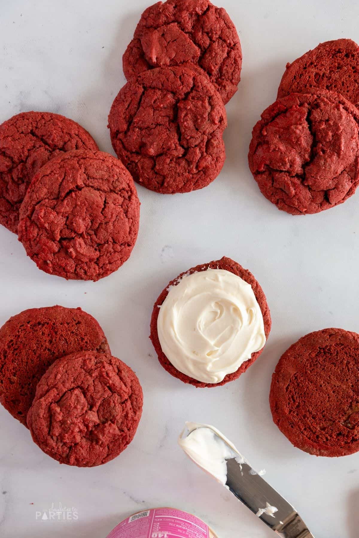 Red cookies paired up around a single cookie with frosting spread on the bottom.
