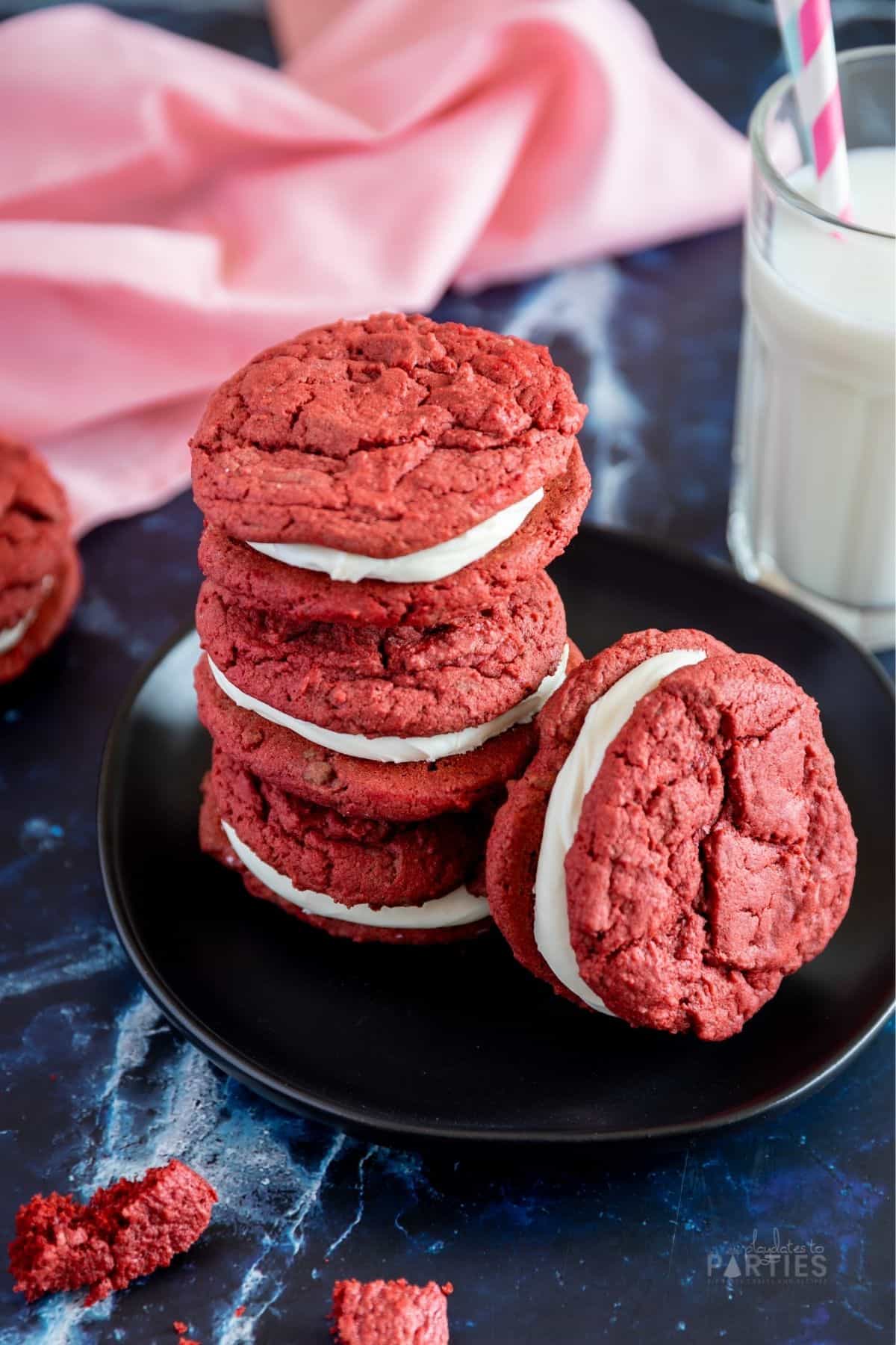 Red velvet cookie sandwiches piled on a black plate with a pink napkin in the background.
