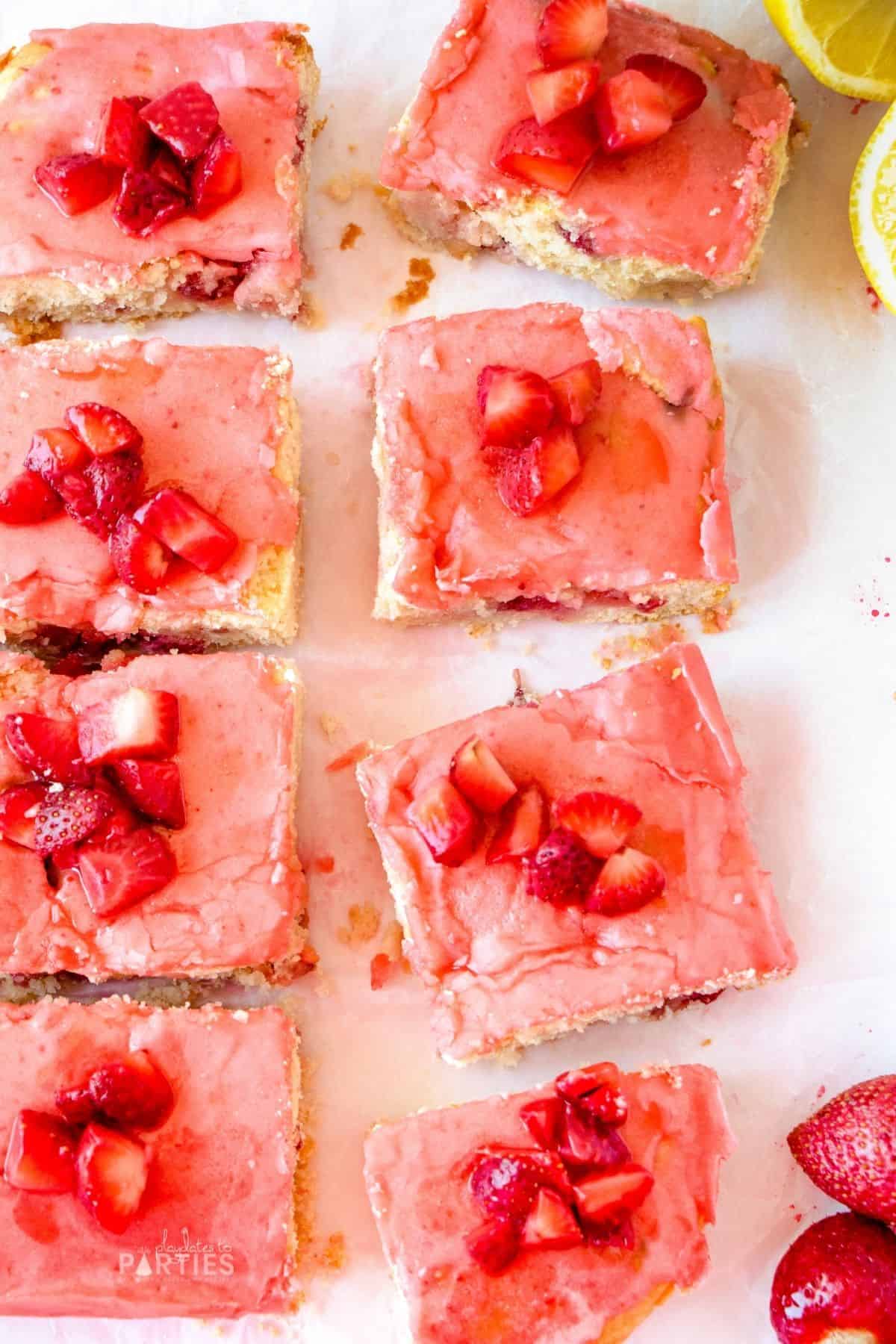 Overhead view of lemon bars covered with strawberry glaze on a white surface.