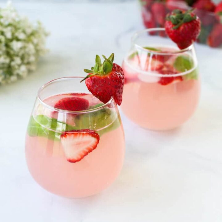 Two pink strawberry mocktail spritzers on a marble surface.